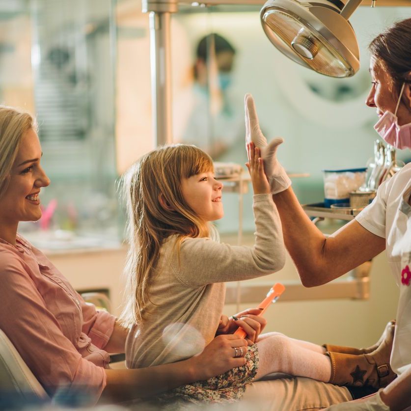 Happy girl with her mother giving high five to a dentist after medical exam at dentist's office.