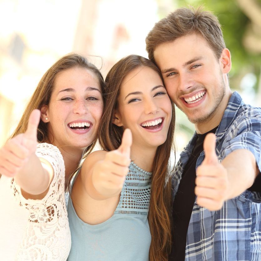 Three happy friends smiling with thumbs up in the street